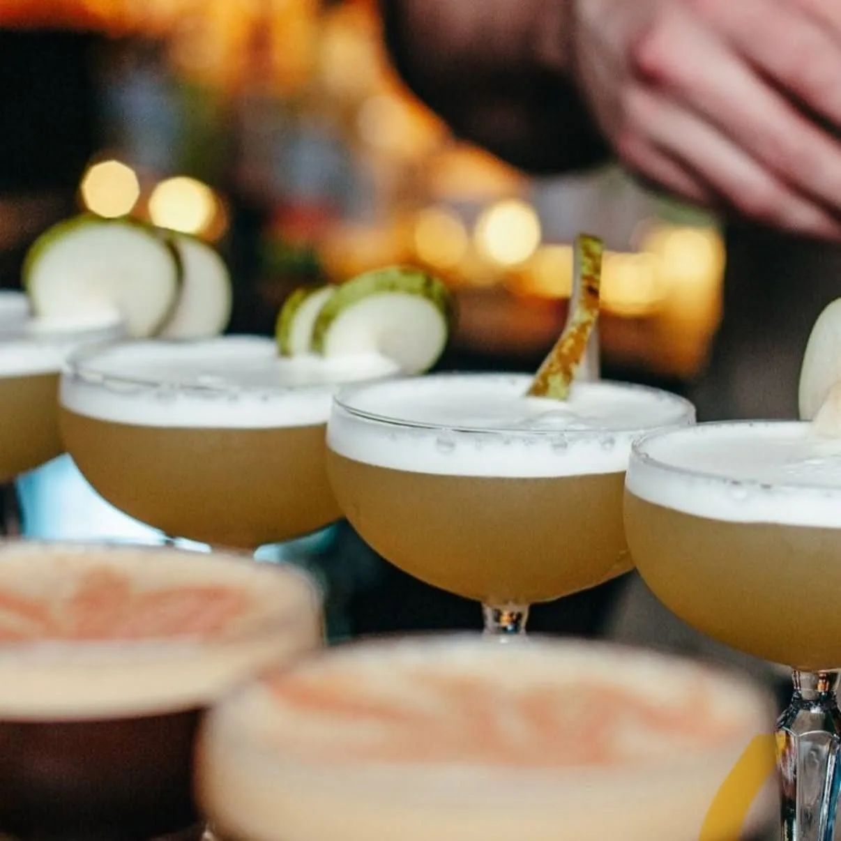 Row of frothy sour cocktails garnished with apple at The Old Workshop cocktail bar in Aberdeen